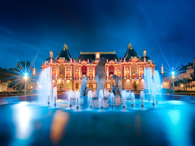 Photo du palais des beaux art de Lille prise à l'heure bleue en pose longue ce qui amène une douceur avec les jets de la fontaine devant. La couleur bleu mets en valeur la teinte orangée du palais des beaux art de lille. Photo palais des beaux art Lille